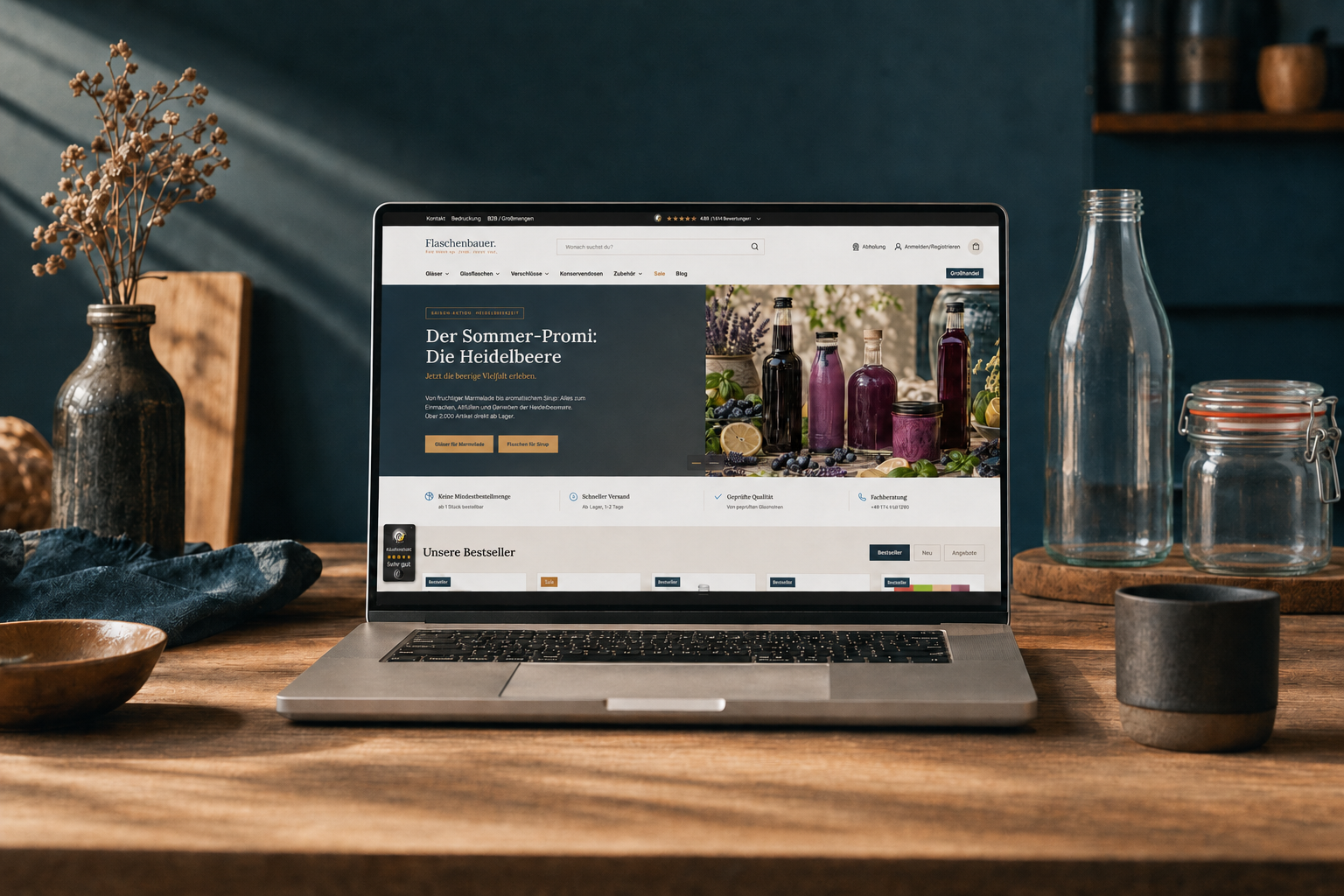 Geöffneter Laptop mit der Flaschenbauer-Homepage und Heidelbeer-Aktionsbanner, daneben eine klare Milchflasche und ein Drahtbügelglas auf einem Holztisch